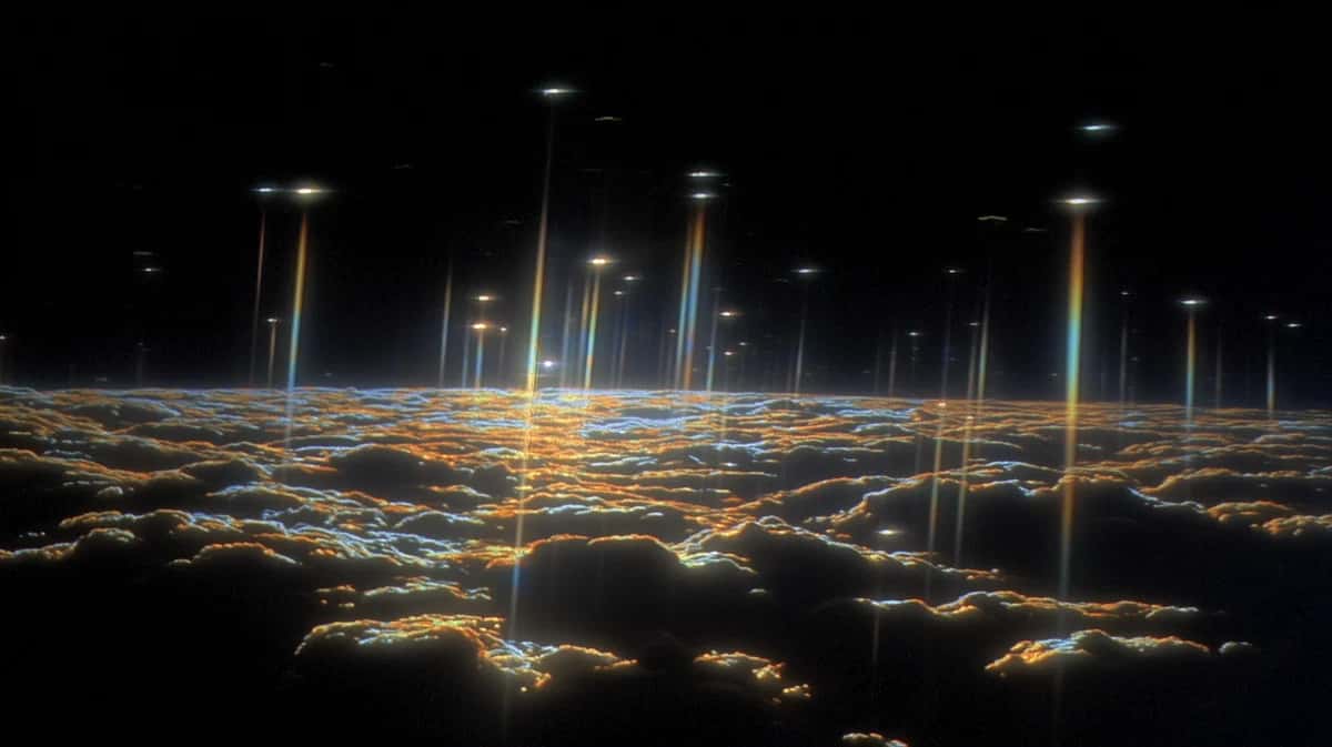 Aerial view of glowing city lights at night above clouds, golden and blue illuminated landscape